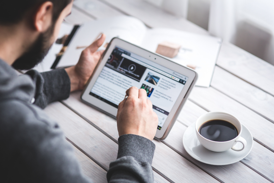 A man reading the news on a tablet at a table with a coffee cup.