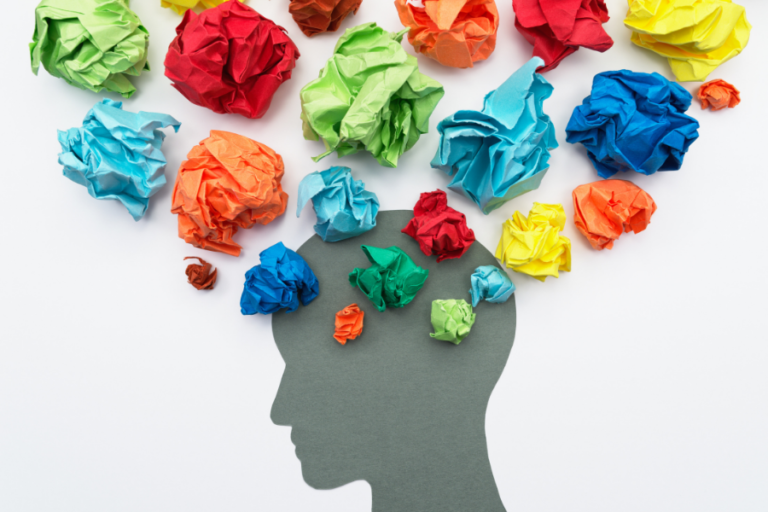 A shadow of a human head with crumpled colorful paper coming out of the top.