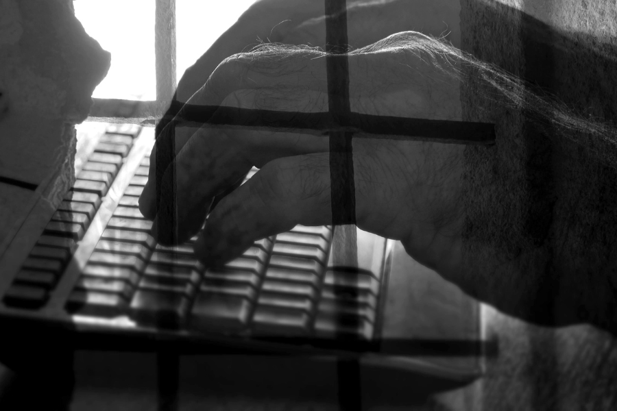 An image of hands typing on a keyboard with an overlay of prison bars over top of it.